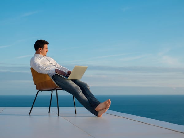 handsome young man relaxing and working on laptop computer at home balcony while looking sunset